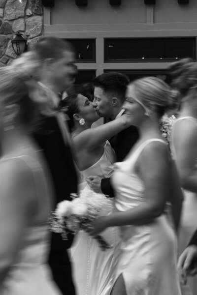Minnesota Wedding Photography | Black and White photo of bride and groom kissing with the wedding party blurry around them 