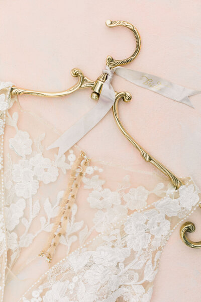 Lace sleeveless wedding dress on a brass vintage hanger from Anthropologie with a silk ivory ribbon tag that says "Bride" in modern calligraphy