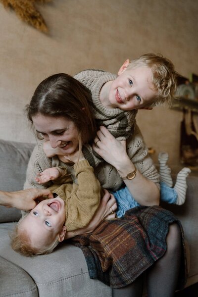 Mama en zoontjes stoeien op de bank tijdens gezinsfotoshoot