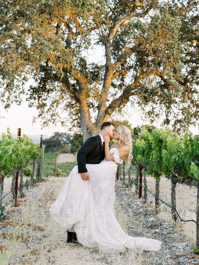 a bride holding a bouquet of overflowing fall flowers on her wedding day at a California vineyard.