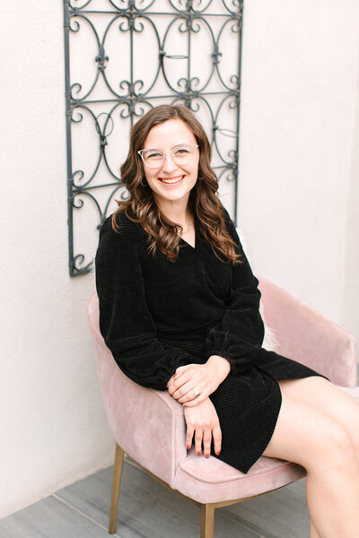 Kalie Breeze, general manager of SoHo63, a Chandler wedding and event venue, smiles while standing in front of a modern white cityscape backdrop. Her professional and friendly demeanor reflects the exceptional service and hospitality SoHo63 is known for.