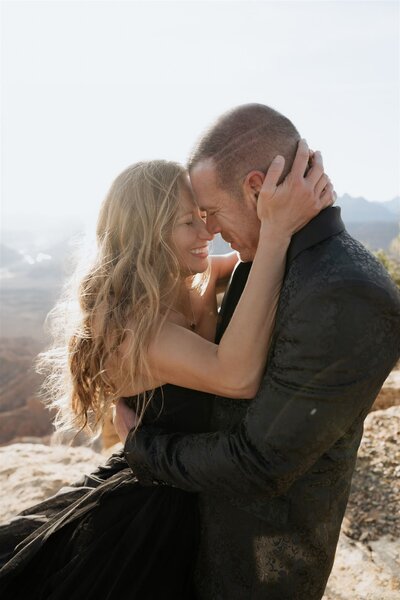 Couple closely embracing in joy during their elopement in the mountains with the sun backlighting them.