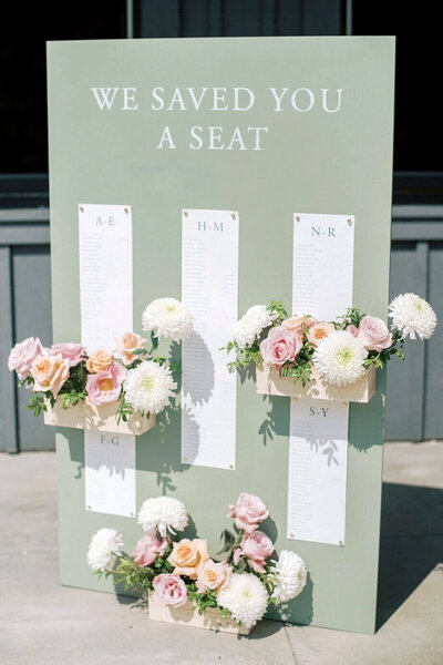 Custom wooden seating chart for a pastel wedding at Moonlight Basin, featuring acrylic letters and flower boxes filled with soft blush, white, and peach florals.