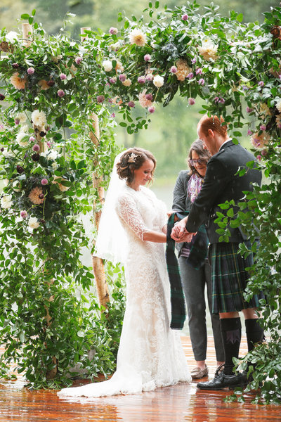 jewish and scottish couple combines their traditions for their private estate wedding chuppah is covered with greenery and flowers designed by roots floral design on a lakefront dock