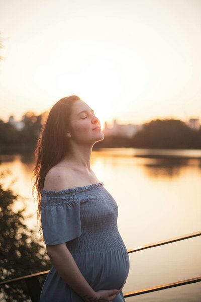 Pregnant woman gazing out over a calm lake, representing deeper trauma healing through a 3-day EMDR Intensive
