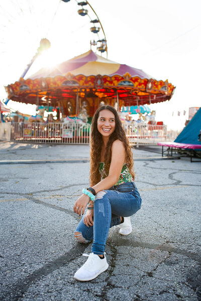 Senior portrait of a girl at a fair in front of a carousel