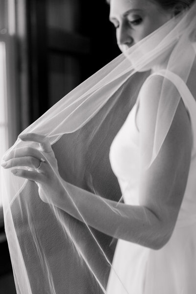 Black and white photo of a bride holding her veil