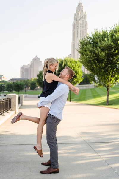 A young man lifts his fiance with the Columbus skyline in the background