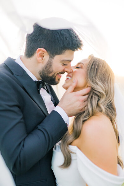 Well dressed couple kissing at the alter with an arbor of flours behind them.