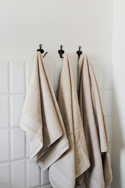 A white tile wall with hooks holding bath towels.