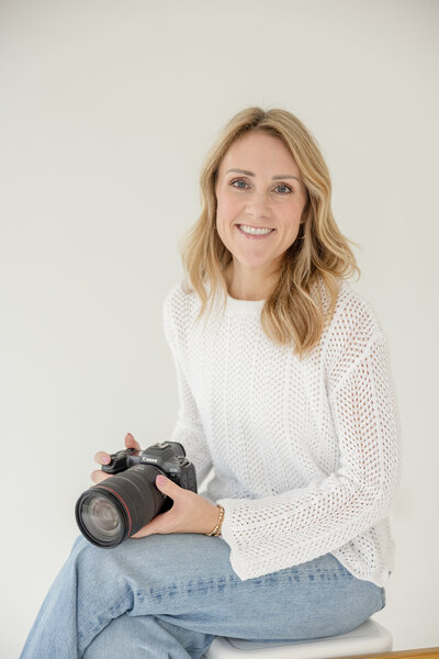 Mother holding her baby up in front of a rose covered trellis.
