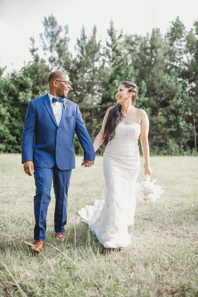 Newlyweds walk hand in hand, laughing in a scenic outdoor venue. Beautiful moment by Jackson Ms Wedding Photographer.