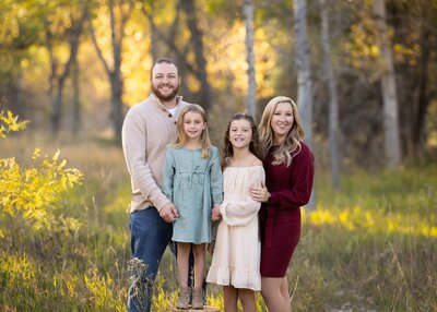a family of four with two young girls standing together in a forest
