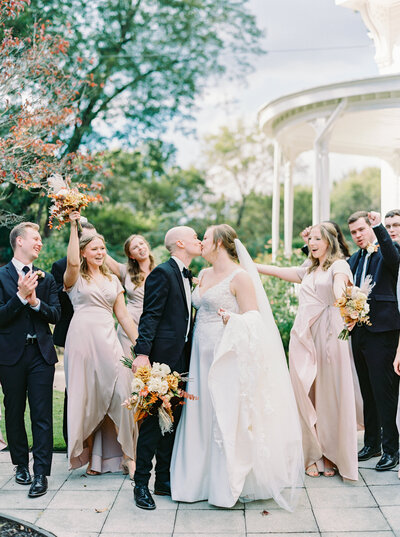 Bride and groom kissing with bridal party cheering