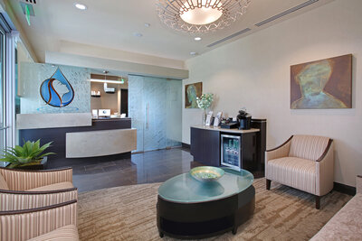Modern plastic surgery office featuring contemporary lighting, high-end design, textured glass with custom logo, and a coffee bar, designed by EnviroMed Design. The space creates a welcoming and inviting atmosphere for patients.