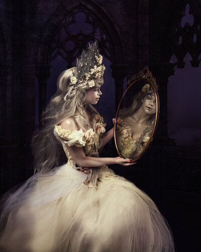 Young woman in a designer gown for a couture portrait wearing a crown holding a mirror seeing her reflection