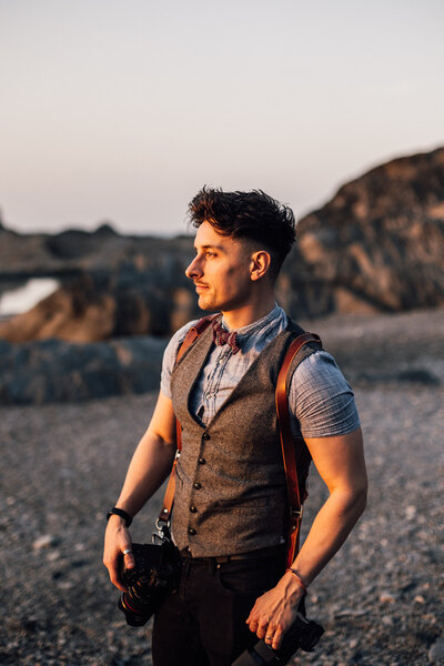 Ollie dressed in a vest and standing cliffside with camera
