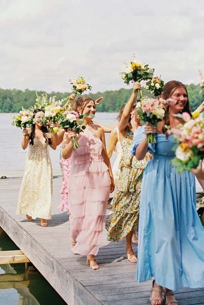 girls in dresses walking down boardwalk holding flowers in the air