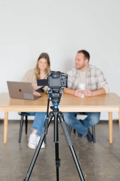 brand photographer offers content creation service with two people sitting at a table with a camera on a tripod in front of them