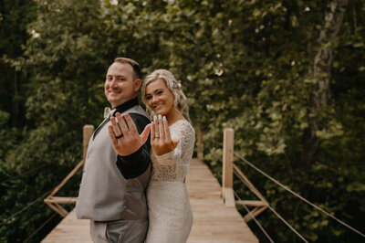 Newlyweds showing off their wedding rings on a wooden bridge