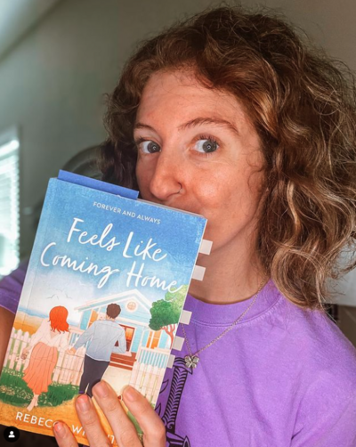 Woman posing for camera holding copy of Feels Like Coming Home by Rebecca Wrights