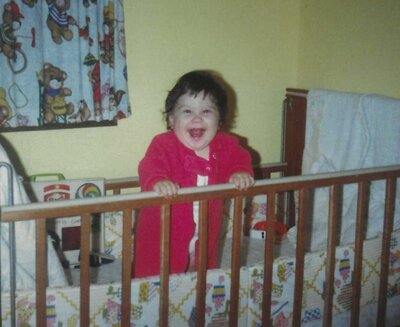 Jen Heller as a child in red pajamas in a crib