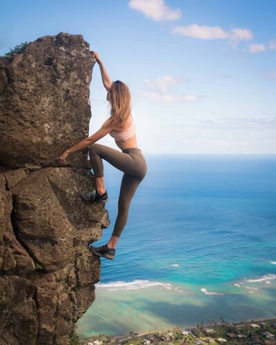 Woman climbing on rocks with blue water below