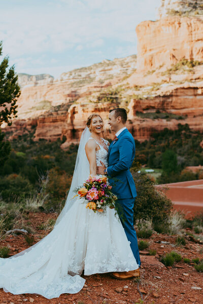 bride and groom stand together with smiles and a sedona backdrop