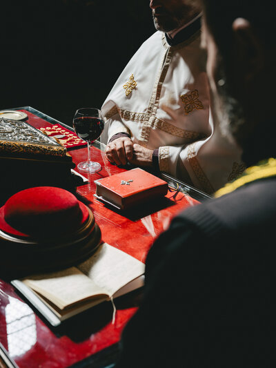 A father's hands lying on a red surface with a wine glass and decorative elements in dark lighting.