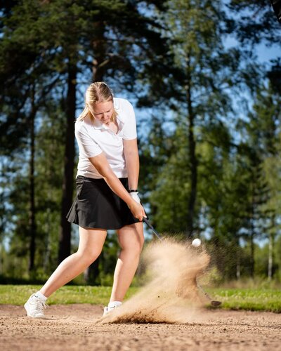 Actionbild av en golfspelare som slår ett bunkerslag.