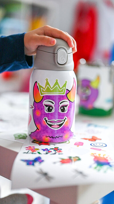 Up close shot of girl's hand on top of a customized Luua water bottle that she decorated with vinyl stickers during a lifestyle product photoshoot.
