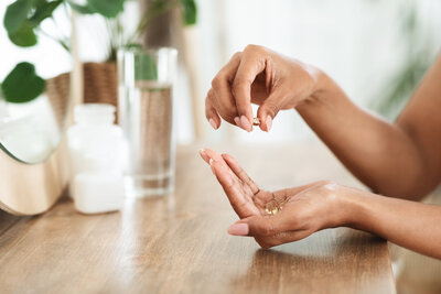 destress multivitamin for moms in woman's hands at wooden table with glass of water
