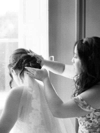 Bridesmaid adjusts brides hair and veil before her wedding