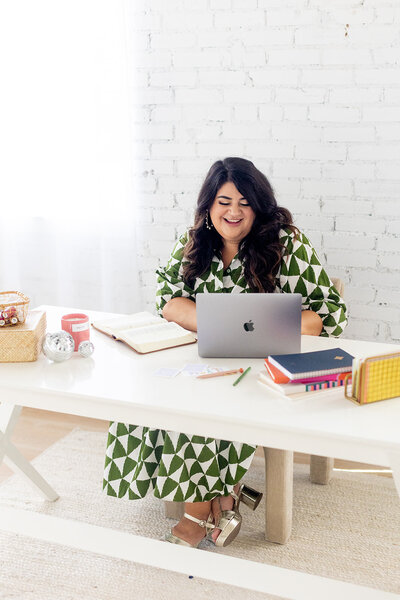 Marissa Martinez in a green and white patterned dress working at a white table with her laptop and Bible