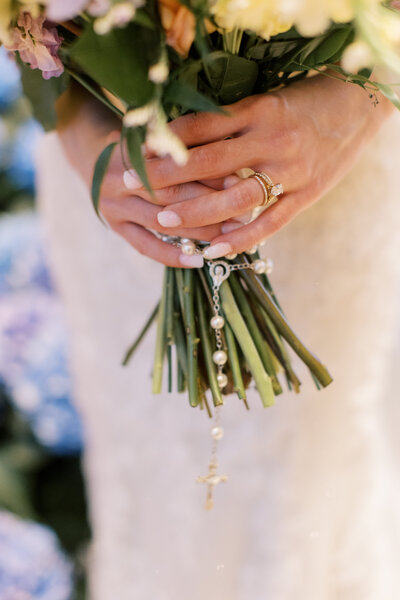 Close up of Catholic bride holding her bouquet with a beautiful rosary wrapped around the stem.