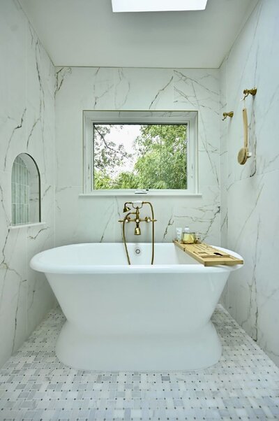 Modern master bath with large skylight, marble surfaces, glass shower, and green vanity with brass finishes.