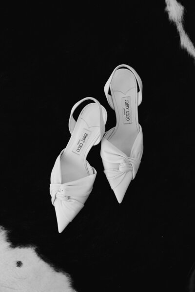 Jimmy Choo White Slingback Pumps sit on a cowhide rug during getting ready photos on a wedding day. 