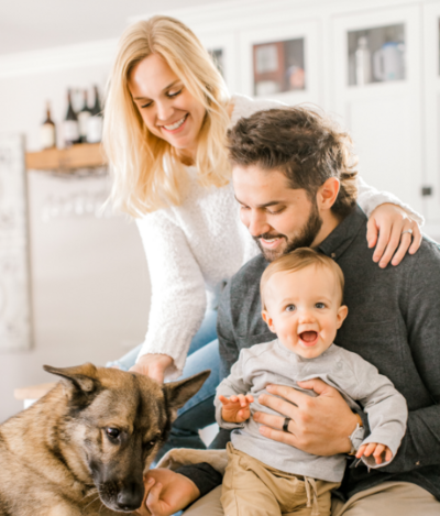 Couple smile at their dog whilst posing with their baby