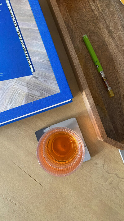 A glass of orange drink beside a blue notebook and a pencil