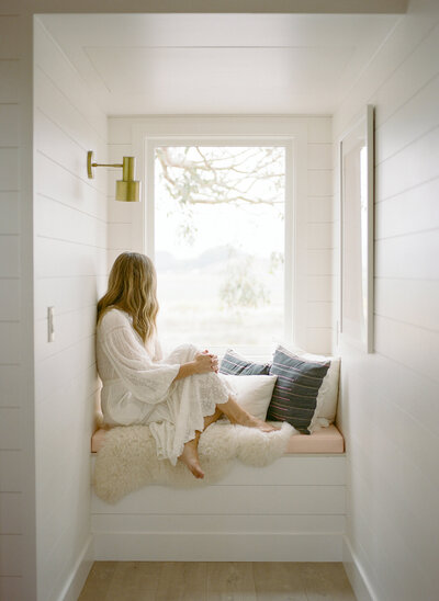 A woman facing the window, exuding serenity and calm, with soft natural light creating a peaceful atmosphere, embodying relaxation and mindfulness after a restorative CFT session.