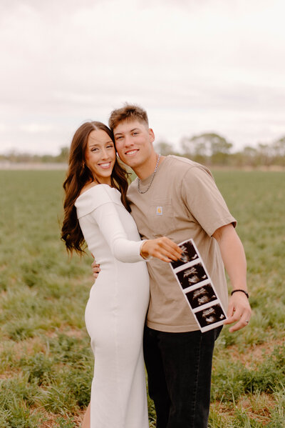 Couple announcing their pregnancy in a grassy field with a sonagram photo