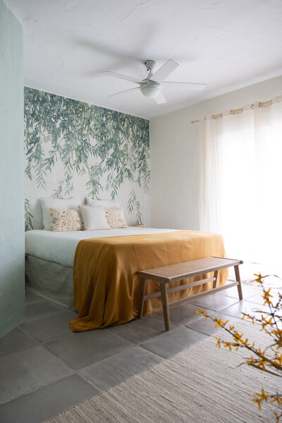 Light and airy B&B room decorated with green leaves on the wall and a ocre color bed linnen and cushions