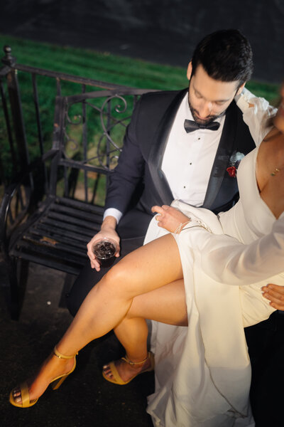 Bride and groom sitting on a bench, the bride’s legs crossed elegantly.