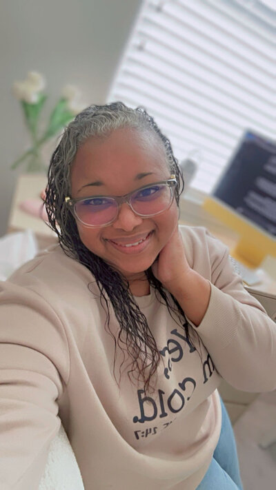 Letitia Hopkins sitting at her desk, smiling confidently, embodying self-love, personal alignment, and Main Character Energy as a life, love, and relationship coach guiding women into empowered lives and relationships.
