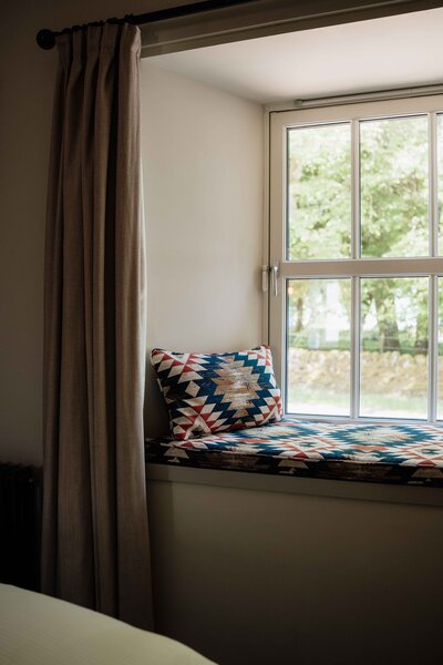 A window sear with bold patterned cushions and neutral curtains.
