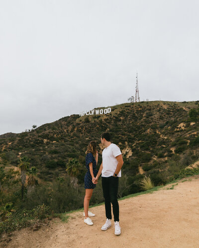 man and woman holding hands with hollywood sign in background