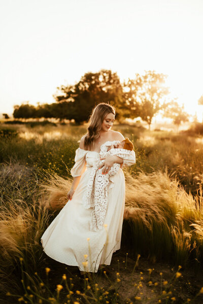 Mom in a gorgeous white dress holding her newborn in the evening glow.