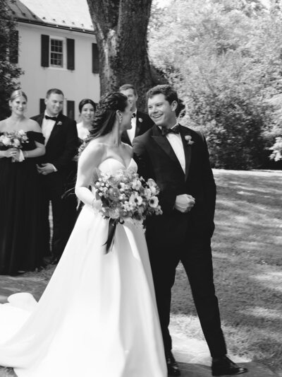 Bride and groom walking arm in arm as they look and smile at each other. 