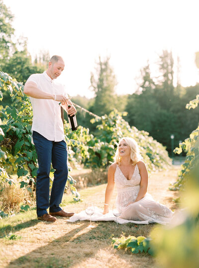 couple laughing popping bottle of wine in the middle of a vineyard in woodinville wa