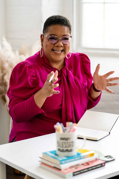 Career coaching for women in leadership, with a professional wearing a branded pink blouse, sitting at a white desk surrounded by office tools like notebooks, pens, and a laptop, symbolizing empowerment and leadership growth.